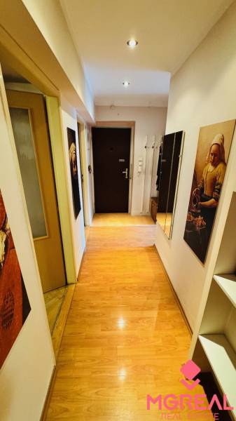 Na predaj 3 i  byt s loggiou aj terasou - Prievidza 75,24 m2 - Úzka chodba s podlahou s dreveným dekorom v 3-izbovom byte, s obrazmi a zrkadlom.