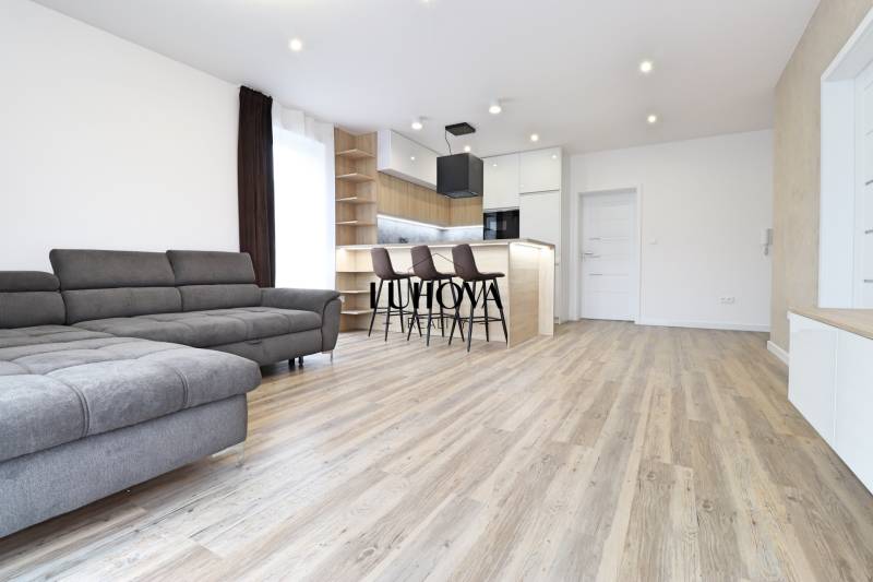 Na PRENÁJOM_v NOVOSTAVBE krásny 3-izbový byt s parkovacím státím - Obývačka v 3-izbovom byte s pohovkou, barom a podlahou s dreveným dekorom.