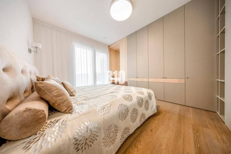 LUXUSNÝ 3-IZBOVÝ BYT NA MIERU V NADČASOVEJ NOVOSTAVBE NA ZAČIATKU KOLI - Spálňa v 3-izbovom byte s posteľou, vstavanou skriňou a podlahou s dreveným dekorom.