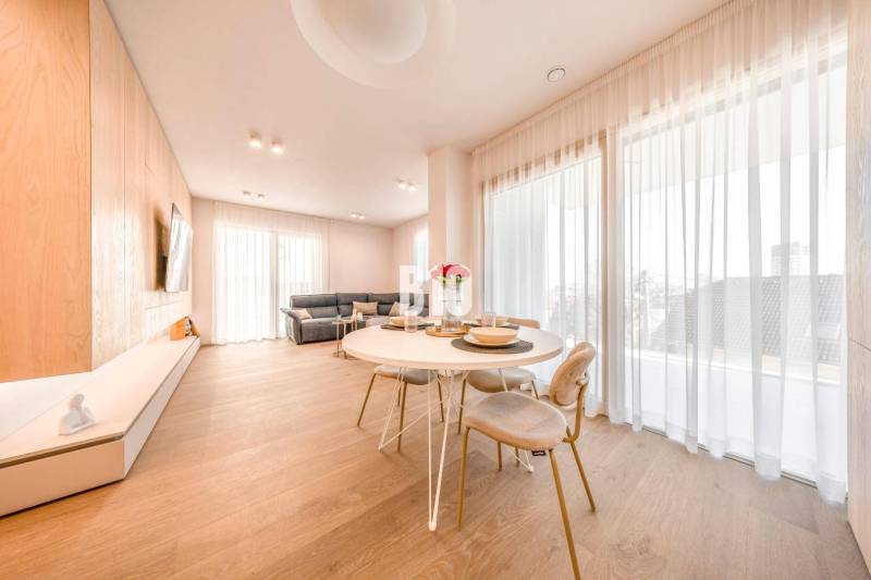 LUXUSNÝ 3-IZBOVÝ BYT NA MIERU V NADČASOVEJ NOVOSTAVBE NA ZAČIATKU KOLI - Obývacia izba v 3-izbovom byte s podlahou s dreveným dekorom, jedálenským stolom a sedačkou.