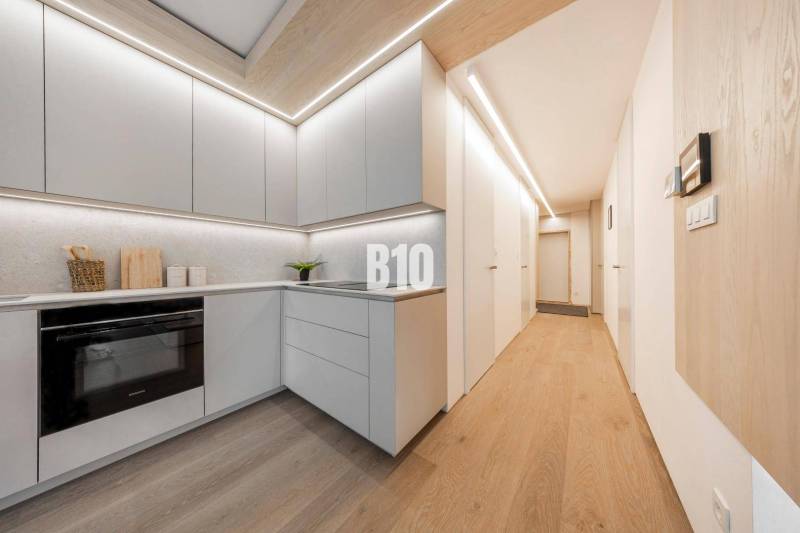 LUXUSNÝ 3-IZBOVÝ BYT NA MIERU V NADČASOVEJ NOVOSTAVBE NA ZAČIATKU KOLI - Kuchyňa v 3-izbovom byte s podlahou s dreveným dekorom a svetlým nábytkom.