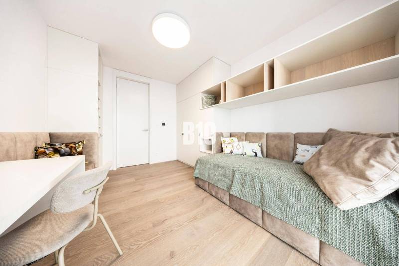 LUXUSNÝ 3-IZBOVÝ BYT NA MIERU V NADČASOVEJ NOVOSTAVBE NA ZAČIATKU KOLI - Minimalistická izba s pohovkou, svetlým nábytkom a podlahou s dreveným dekorom v 3-izbovom byte.