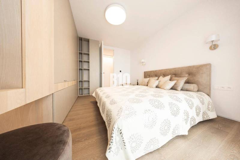 LUXUSNÝ 3-IZBOVÝ BYT NA MIERU V NADČASOVEJ NOVOSTAVBE NA ZAČIATKU KOLI - Svetlá spálňa s podlahou s dreveným dekorom a zabudovanými skriňami v 3-izbovom byte.