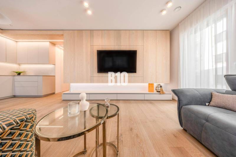 LUXUSNÝ 3-IZBOVÝ BYT NA MIERU V NADČASOVEJ NOVOSTAVBE NA ZAČIATKU KOLI - Obývacia izba v 3-izbovom byte s podlahou s dreveným dekorom a televízorom na stene.