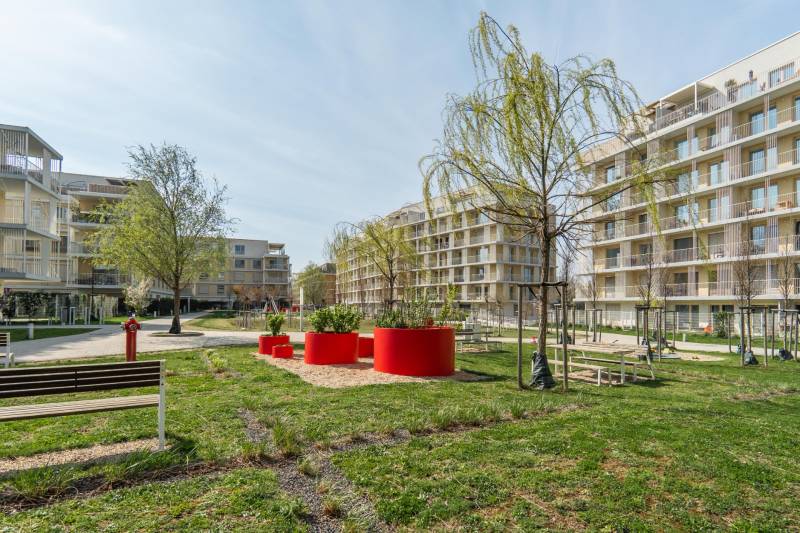 Bývanie ako z katalógu – Dizajnový 3-izbový byt s terasou a parkovaním - Exteriér bytových domov v Bratislave - Ružinove so stromami a lavičkami.