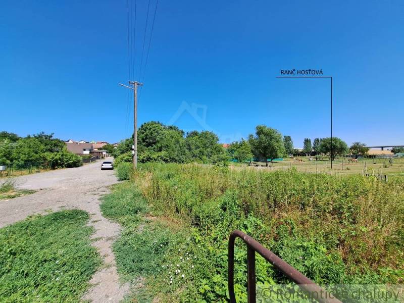 Stavebný pozemok pri Nitre so stavebným povolením v tichej lokalite - Cesta vedie k Pozemkom - bývanie v Hosťovej s výhľadom na zeleň a domy.