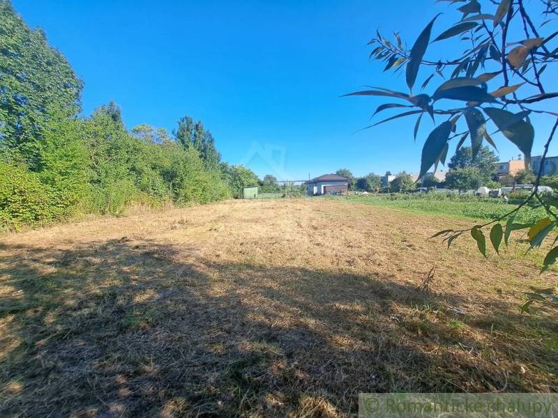 Stavebný pozemok pri Nitre so stavebným povolením v tichej lokalite - Pozemok na bývanie obklopený zeleňou v Hosťovej za slnečného počasia.