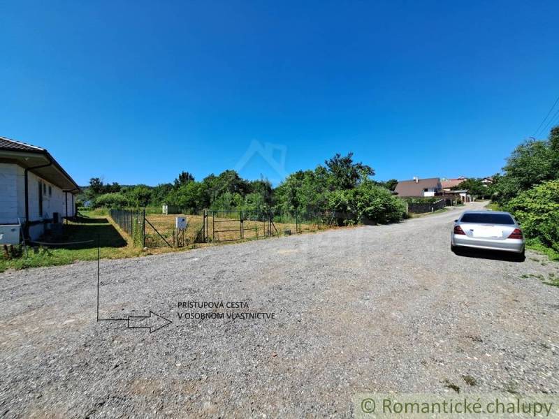 Stavebný pozemok pri Nitre so stavebným povolením v tichej lokalite - Pozemky - bývanie v Hosťovej: štrková cesta, oplotený pozemok, vedľa zaparkované auto.