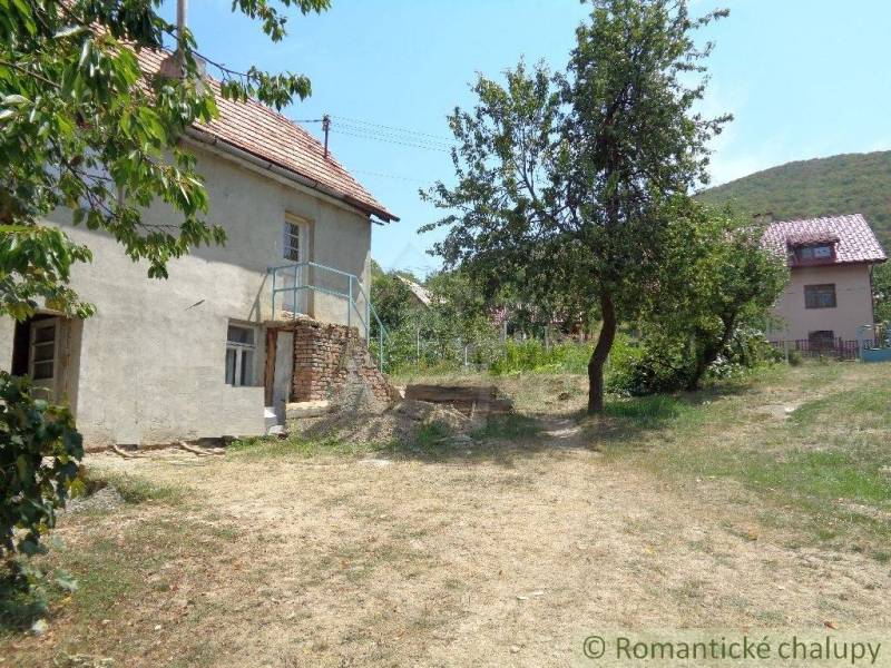 CENA DOHODOU Menší domček v príjemnom prostredí obce Šiatorská Bukovin - Rodinný dom v Šiatorskej Bukovinke so záhradou a stromami pod modrou oblohou.