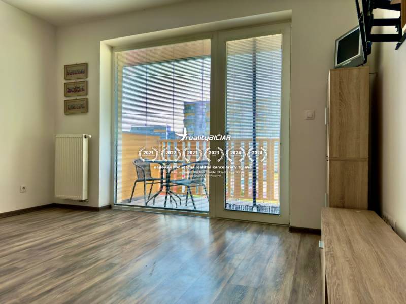 Na predaj moderný 2 izbový byt, komplex MIKO Trnava - Obývacia izba v 2-izbovom byte s podlahou s dreveným dekorom a prístupom na balkón.