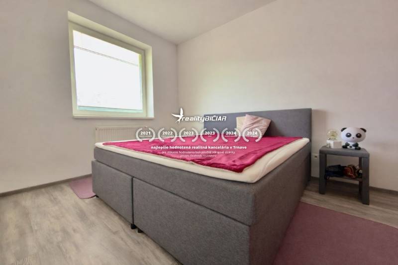 Na predaj moderný 2 izbový byt, komplex MIKO Trnava - Spálňa v 2-izbovom byte s posteľou, podlahou s dreveným dekorom a nočným stolíkom.