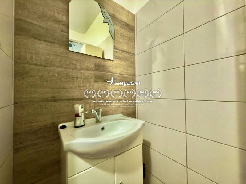 Na predaj moderný 2 izbový byt, komplex MIKO Trnava - Kúpeľňa v 2-izbovom byte s umývadlom a zrkadlom, stena s dreveným dekorom.