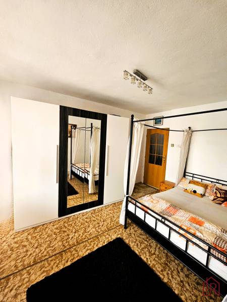 Predaj 5-izbový dom v Kameňanoch, okres Revúca - Spálňa v rodinnom dome s posteľou, kobercom a skriňou so zrkadlom.