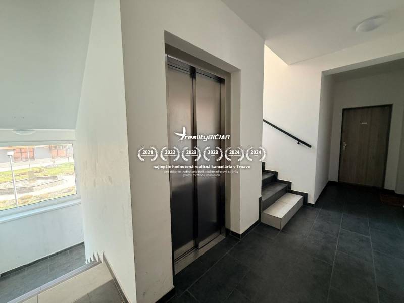 Na predaj moderný 2 izbový byt, komplex MIKO Trnava - Chodba s výťahom a schodiskom v 2-izbovom byte, podlaha s dreveným dekorom.