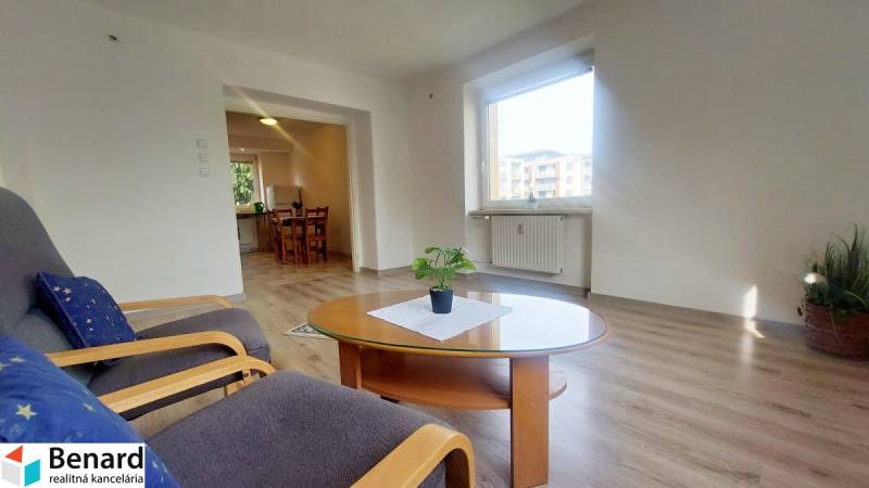 Na PRENÁJOM, VEĽKÝ 2 izb. TEHLOVÝ BYT, SÍDLISKO II., PREŠOV  - Obývačka 2-izbového bytu s oknom, podlaha s dreveným dekorom a stolíkom s rastlinou.