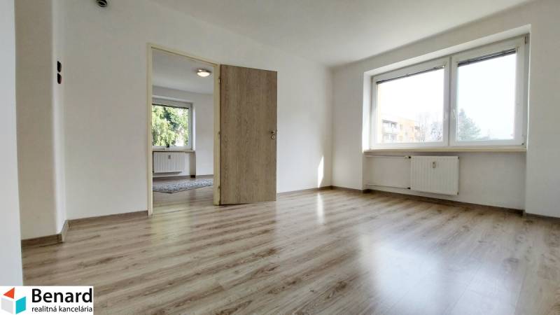 Na PRENÁJOM, VEĽKÝ 2 izb. TEHLOVÝ BYT, SÍDLISKO II., PREŠOV  - Dvojizbový byt s podlahou s dreveným dekorom, veľkým oknom a bielymi stenami.