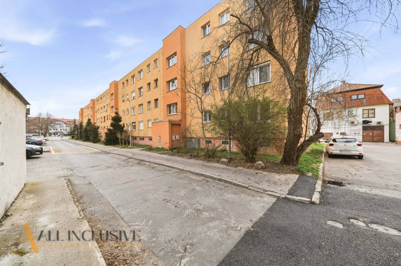 Na predaj 4-izb. byt s loggiou , Dunajská Streda - Exteriér na Radničnom námestí v Dunajskej Strede so žltou obytnou budovou a autami.