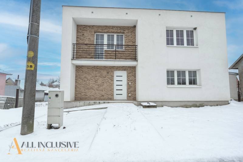 Na predaj poschodový 6-izbový rodinný dom, Horné Mýto - Rodinný dom v Hornom Mýte so snehovou pokrývkou a tehlovými detailmi na fasáde.