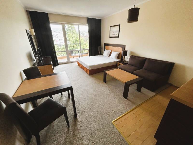 Štúdio DIT Majestic Beach Resort v 1. línií pri mori Bulharsko  - 1-izbový byt so svetlou obývačkou, tmavým nábytkom a podlahou s dreveným dekorom.