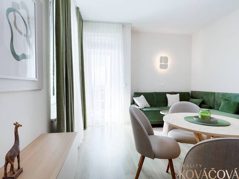 Na predaj 3 izbový byt s terasou, Trenčín, ul. Saratovská - Obývacia izba s podlahou s dreveným dekorom, zelenou sedačkou a jedálenským stolom v 3-izbovom byte.