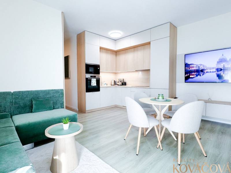 Na predaj 3 izbový byt s terasou, Trenčín, ul. Saratovská - Obývacia časť 3-izbového bytu s podlahou s dreveným dekorom a zeleným gaučom.