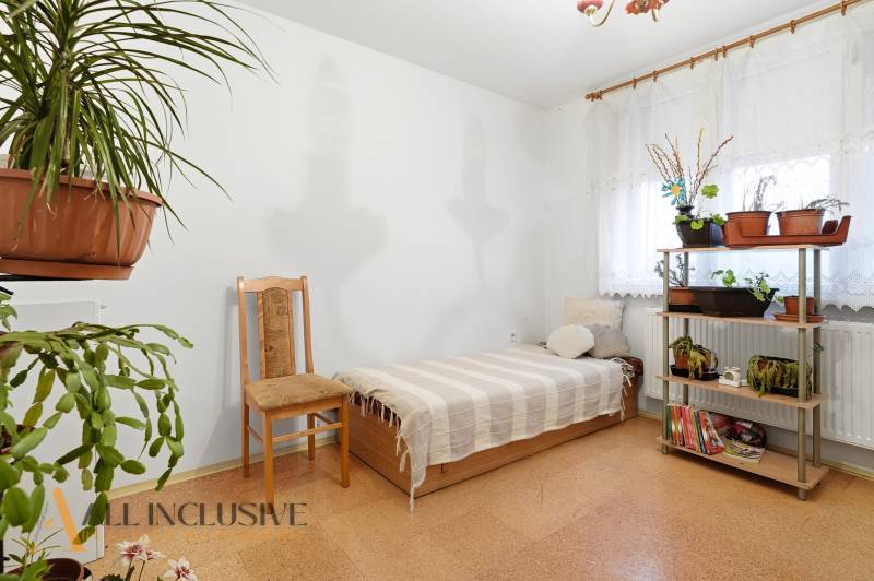 Na predaj 4-izb. rodinný dom s garážou, Okoč - Izba s posteľou a rastlinami v rodinnom dome; podlaha s dreveným dekorom.