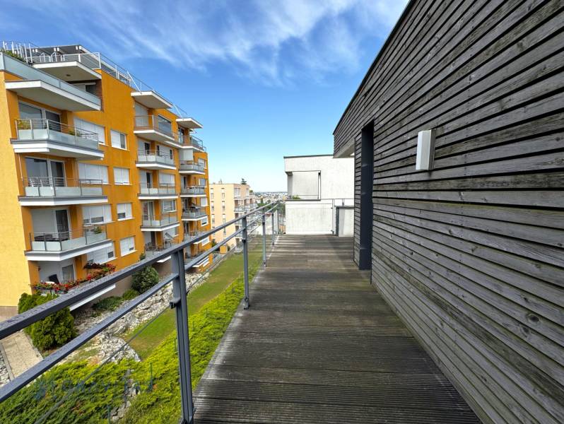 Na predaj veľký 2-izbový byt s terasou a wellness - Koliba - Balkón s drevenou podlahou a výhľadom na bytové domy na ulici Tupého v Bratislave.