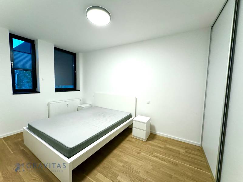 Budova s 8 apartmánmi alebo medicínske centrum - Spálňa s posteľou, vedľa sú dve okná, zasahuje sem umelý osvetlenie stropným svietidlom.