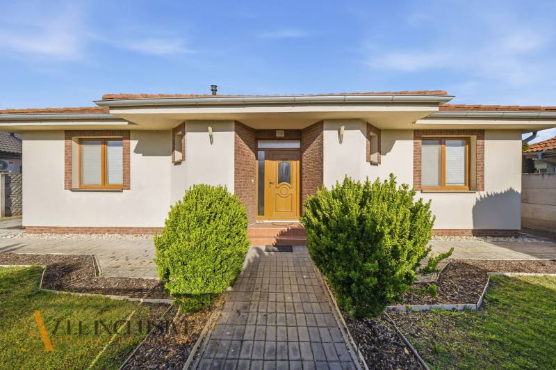 Na predaj 4-izb. rodinný dom s garážou, Kútniky - Rodinný dom v Kútnikoch s kríkovou výsadbou, bielou fasádou a hnedými doplnkami.