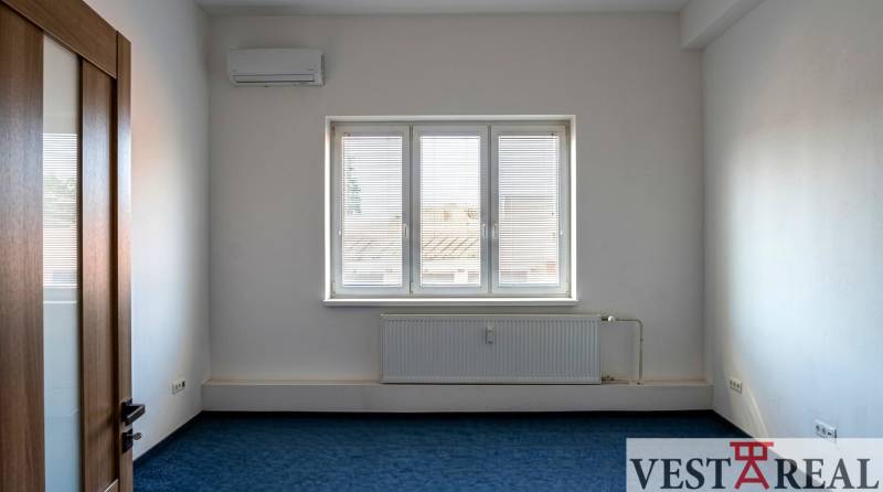 Prenájom klimatizovaná kancelária: 25 m2 a 42 m2 - Trnava Chovateľská - Izba s klimatizáciou a oknom v Kanceláriách, modrý koberec, biele steny.