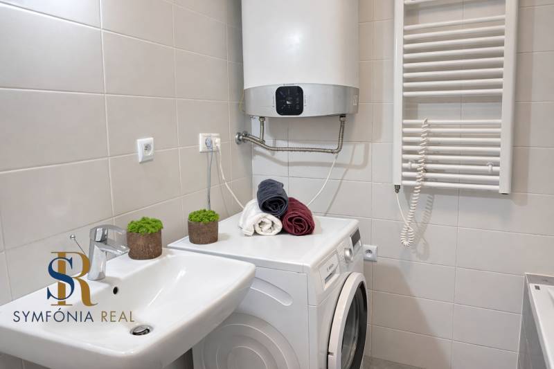 NOVOSTAVBA (2019) + PARKOVANIE | 2-izbový byt 69 m² – Bratislava - Kúpeľňa s práčkou v 2-izbovom byte, bielymi obkladmi a uterákmi.