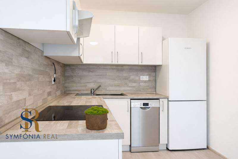 NOVOSTAVBA (2019) + PARKOVANIE | 2-izbový byt 69 m² – Bratislava - Kuchyňa s bielymi skrinkami, spotrebičmi a podlahou s dreveným dekorom v 2-izbovom byte.