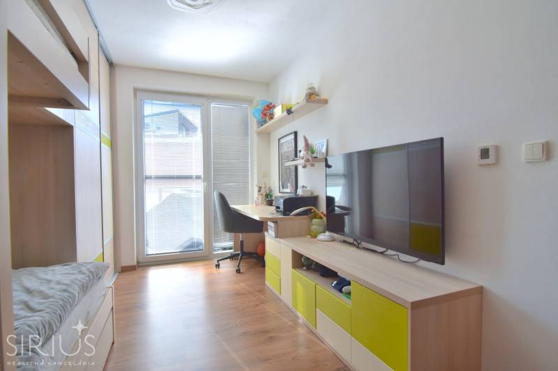 UHLISKÁ, 3-i byt, 80 m2 – zariadená novostavba s parkovaním v cene - Izba s podlahou s dreveným dekorom, pracovným stolom a televízorom v 3-izbovom byte.