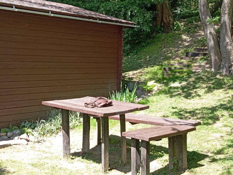 TURANY- krásna chata na pozemku 700m2 - Drevený stôl so stoličkou vedľa chaty, na ulici Černík. Lesná atmosféra, slnečný deň.