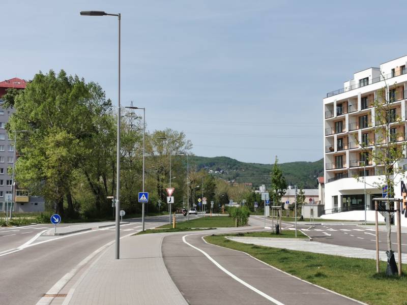 PRENÁJOM parkovacieho miesta v garáži, Rača- RNDZ - Na ulici Eduarda Wenzla, sú stromy, budova a garáže pozdĺž cesty.