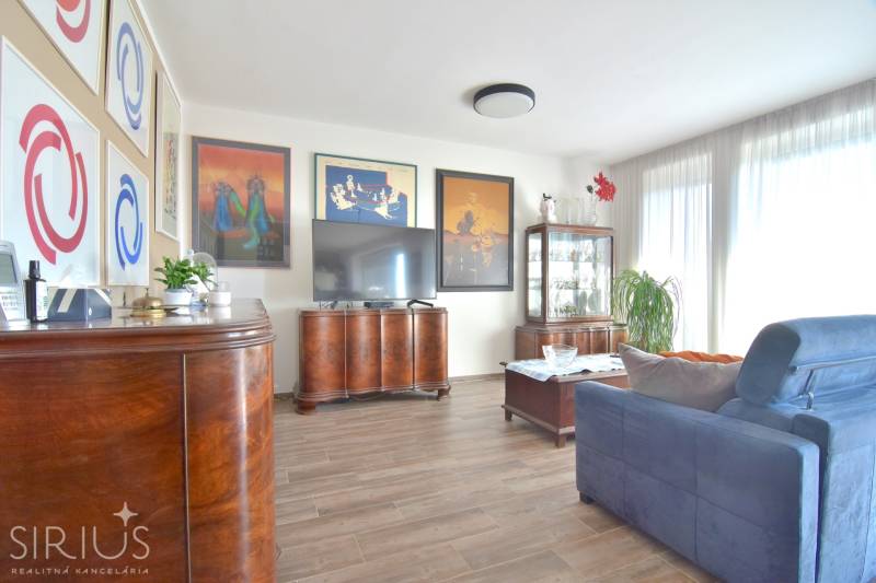 PRI VINOHRADOCH, 3-i byt s veľkými loggiami, 113 m2, RAČANY BIANCO - Obývacia izba s tmavým nábytkom, podlahou s dreveným dekorom a dekoratívnymi obrazmi v 3-izbovom byte.