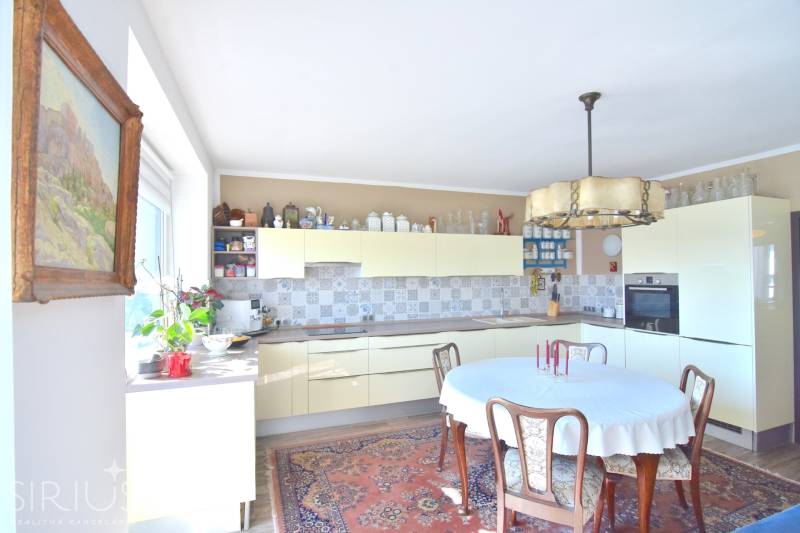 PRI VINOHRADOCH, 3-i byt s veľkými loggiami, 113 m2, RAČANY BIANCO - Kuchyňa v 3-izbovom byte s dreveným nábytkom, kvetinami a vzorovaným kobercom.