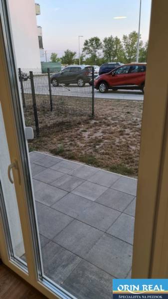 NOVÝ BYT S PREDZAHRADKOU A PARK. STÁTIM - Výhľad z garsónky na uličku Nyárfa v Bratislave - Jarovce s parkovanými autami.