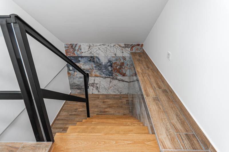 I Predaj štýlového tehlového domu v Rajke pri Bratislave - Interiér rodinného domu so schodiskom, čiernym zábradlím a stenou s dekoratívnym vzorom.