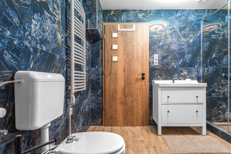 I Predaj štýlového tehlového domu v Rajke pri Bratislave - Kúpeľňa v rodinnom dome s modrými obkladmi, bielou skrinkou a podlahou s dreveným dekorom.