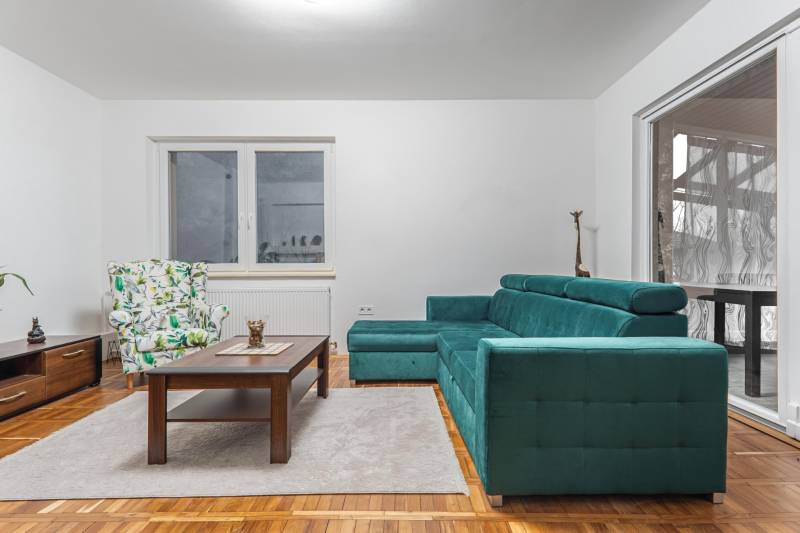 I Predaj štýlového tehlového domu v Rajke pri Bratislave - Obývacia izba so zelenou sedačkou, kreslom s motívom lístia a stolom, v rodinnom dome.