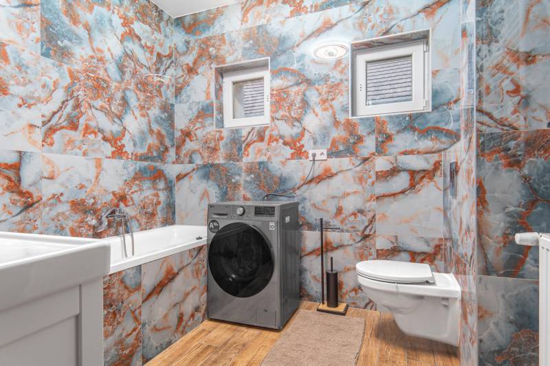 I Predaj štýlového tehlového domu v Rajke pri Bratislave - Kúpeľňa v rodinnom dome s farebnými kachľami, práčka, vaňa a záchod.