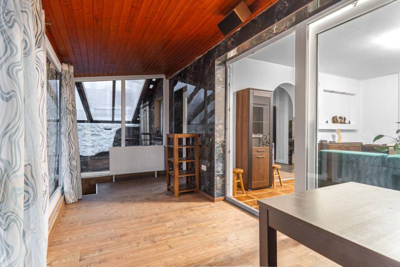 I Predaj štýlového tehlového domu v Rajke pri Bratislave - Interiér rodinného domu s podlahou s dreveným dekorom, presklená stena, závesy, stoličky.