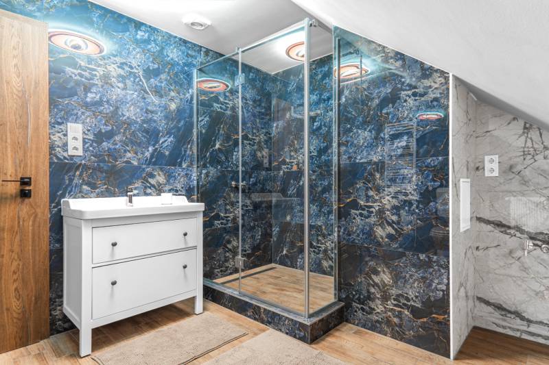 I Predaj štýlového tehlového domu v Rajke pri Bratislave - Kúpeľňa s modrými stenami, sprchovacím kútom a podlahou s dreveným dekorom v rodinnom dome.