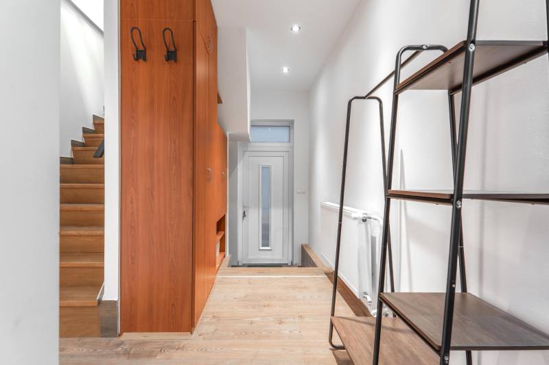 I Predaj štýlového tehlového domu v Rajke pri Bratislave - Chodba v rodinnom dome s podlahou s dreveným dekorom, bielymi stenami a dreveným schodiskom.