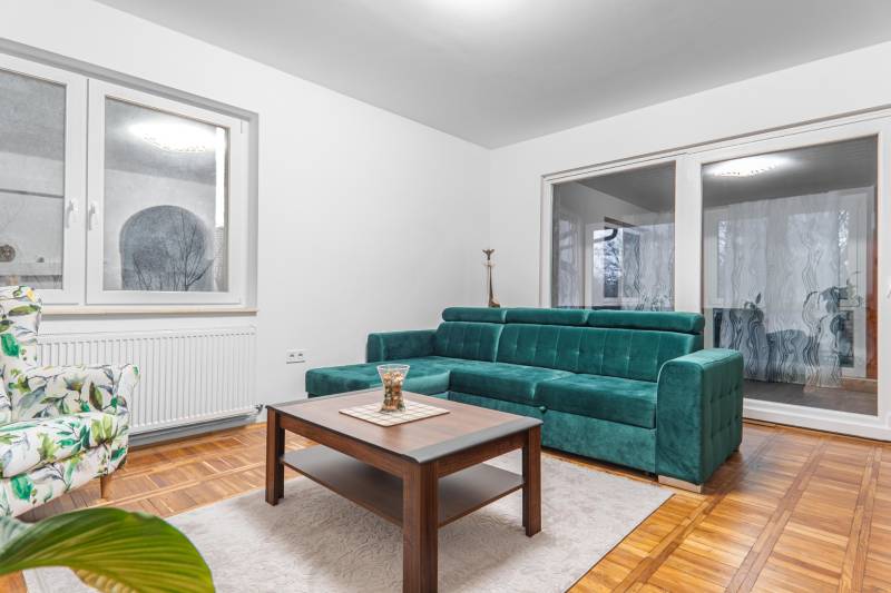 I Predaj štýlového tehlového domu v Rajke pri Bratislave - Obývačka v rodinnom dome s tyrkysovou sedačkou, kvetinovým kreslom a podlahou s dreveným dekorom.