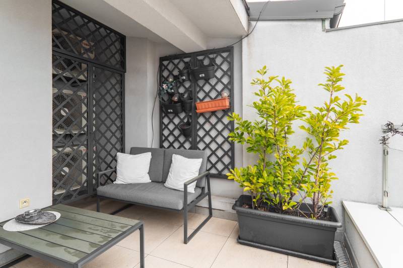 I Exkluzívny penthouse s terasou v absolútnom centre mesta - Balkón v 2-izbovom byte s pohovkou, rastlinami a dekoratívnou mrežovou stenou.