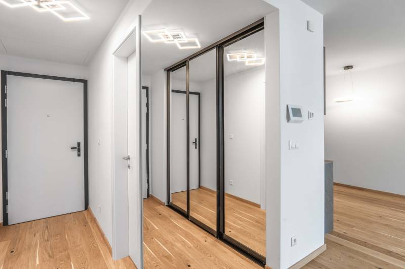 : Nadštandardný 2i byt v projekte ZWIRN za cenu „štandardu“ - Vstupná hala s podlahou s dreveným dekorom a veľkým zrkadlovým šatníkom v 2-izbovom byte.