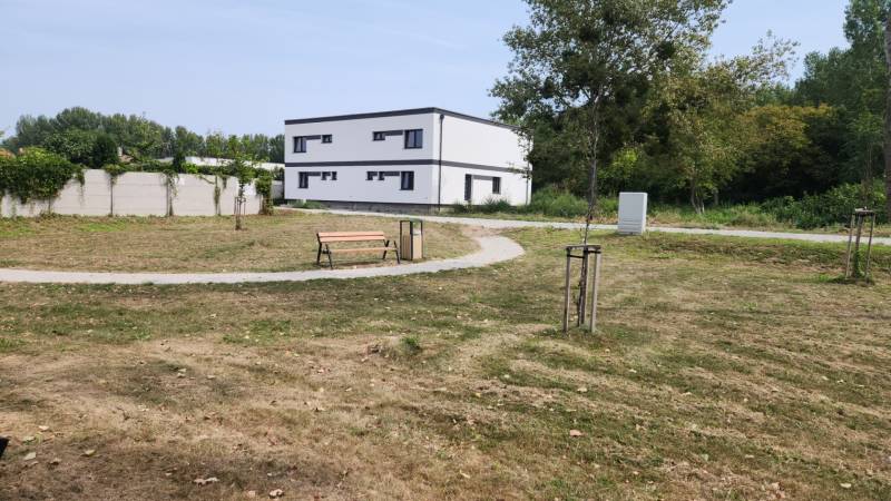 I Predaj 5-i mezonetu s vlastným pozemkom - Park s lavičkou a chodníkom, v pozadí budova v Dunajskom Klátove, 5 a viac izbový byt.