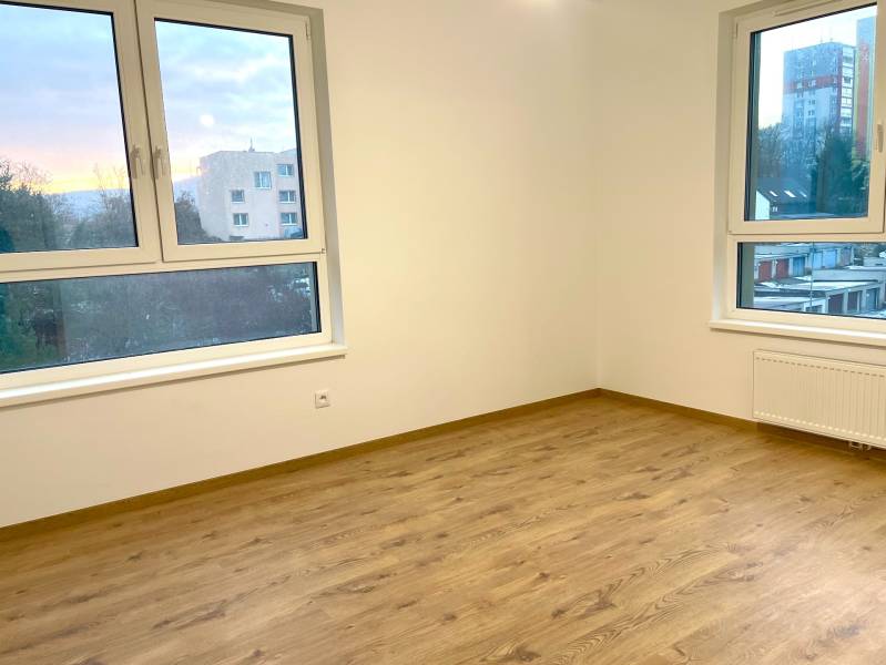 I Predaj 3i bytu v novostavbe v Rači - Prázdna miestnosť s podlahou s dreveným dekorom a veľkými oknami v 3-izbovom byte.